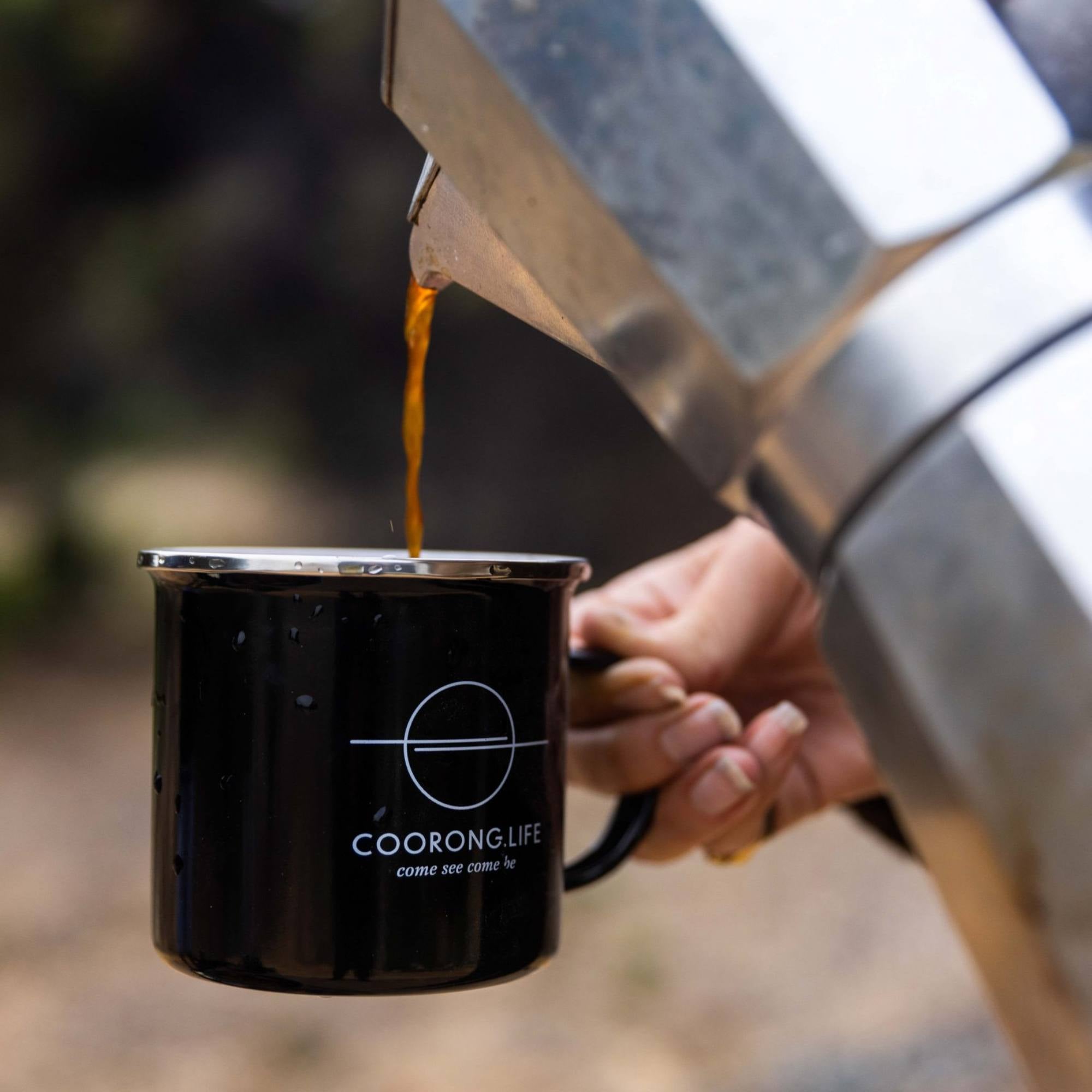 Coffee being poured into a black 'Coorong Life' mug with a blurred natural background
