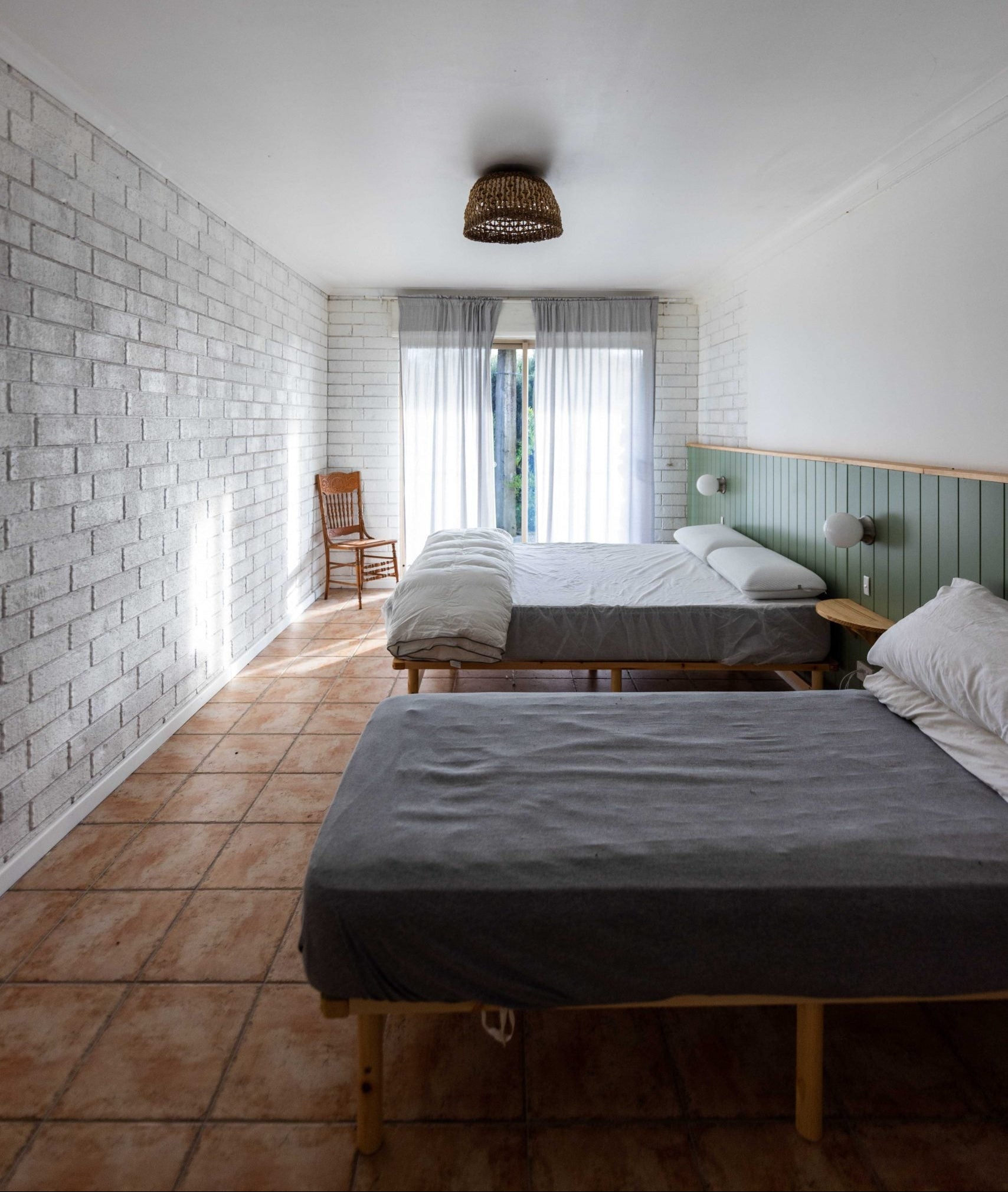 Two beds in a room with a tiled floor and a brick wall. Inside the Art Residency Apt at Coorong Life 