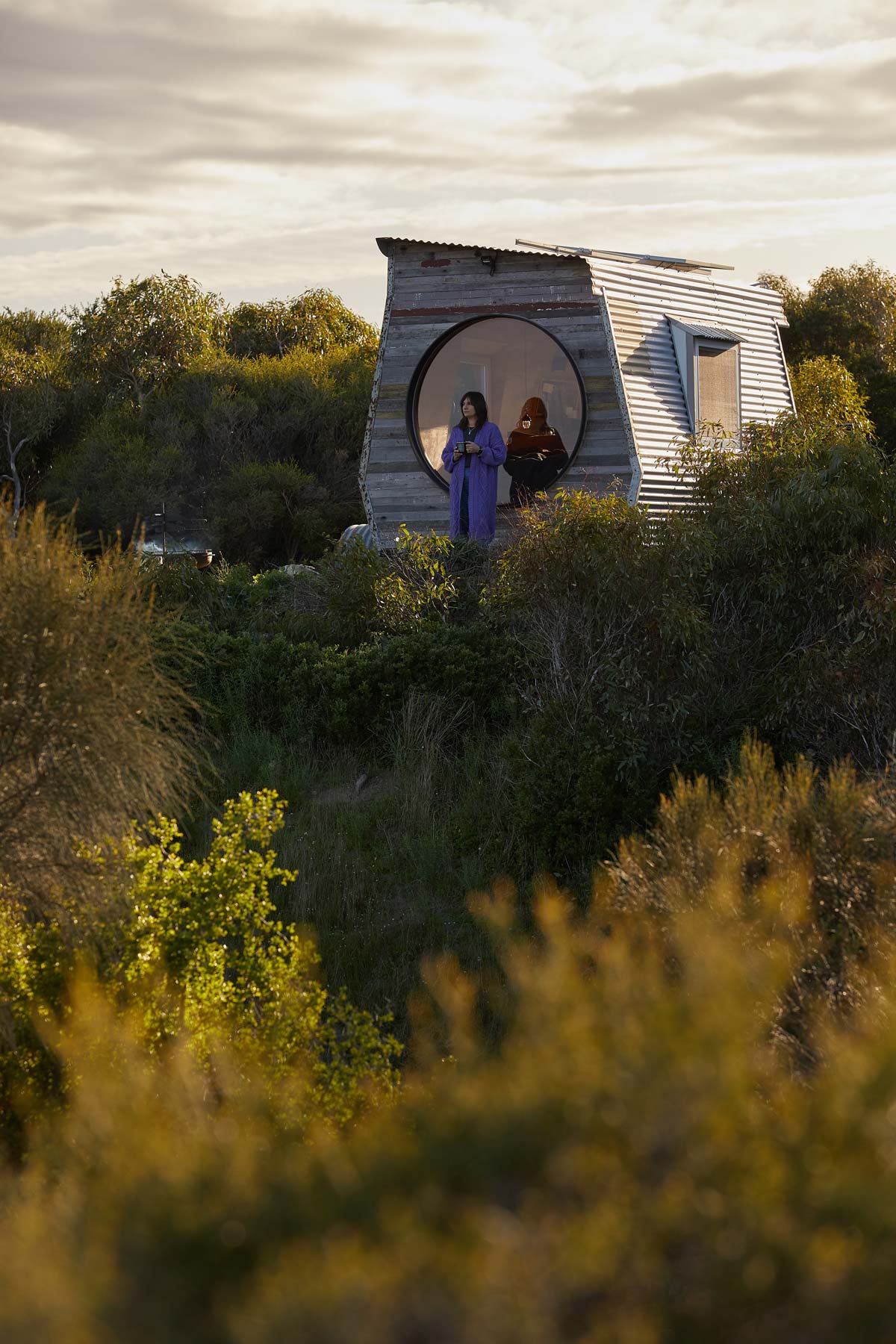 The person standing in front of a circular wooden structure amidst greenery is Kate Brooks the owner of Coorong life in a purple jacket 